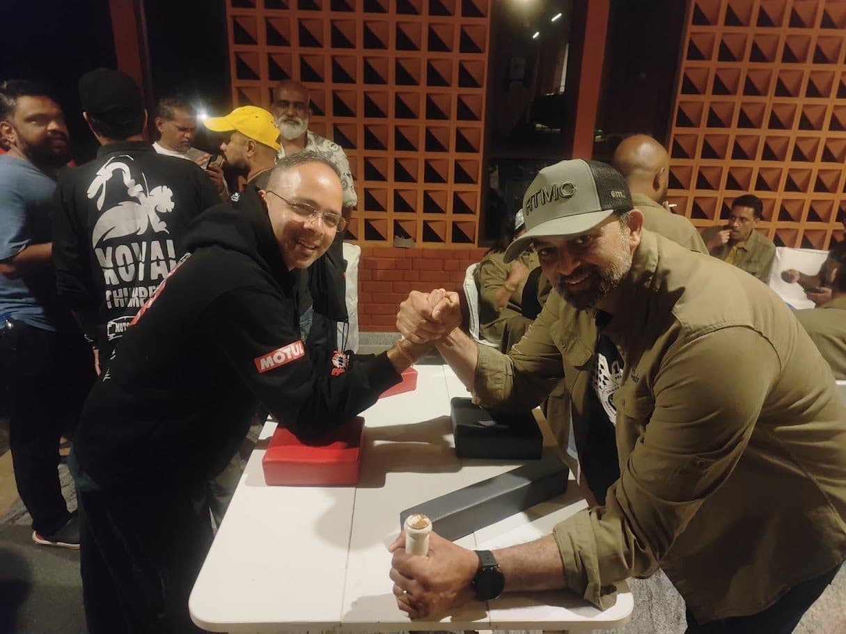 Two RTMC riders arm-wrestling inside the venue, both wearing the XXV merch.